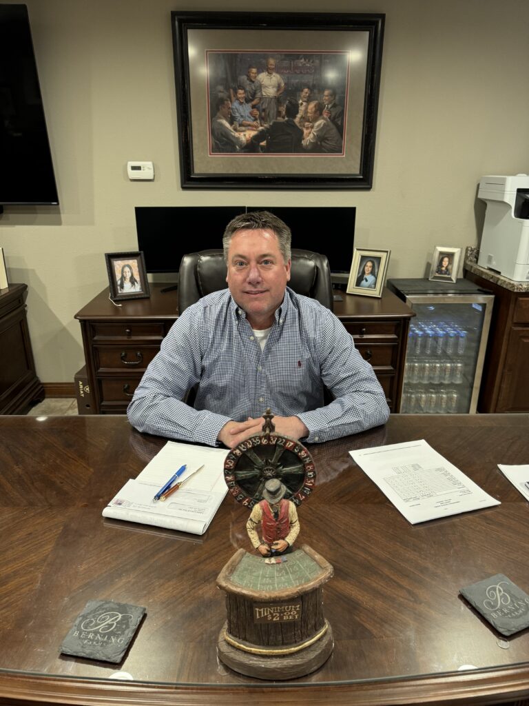 A man sitting at a desk in front of a clock.